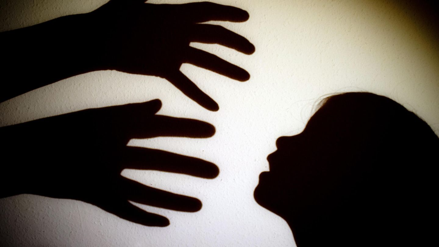 Schatten von Händen einer erwachsenen Person und dem Kopf eines Kindes an einer Wand eines Zimmers