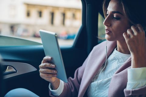 Eine Frau telefoniert mit dem Tablet auf der Rückbank eines Autos