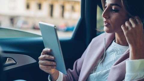 Eine Frau telefoniert mit dem Tablet auf der Rückbank eines Autos