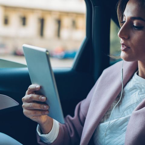 Eine Frau telefoniert mit dem Tablet auf der Rückbank eines Autos