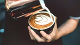 Krebsrisiko Kaffee? Ein Barista schüttet Milch in eine Tasse mit Kaffee