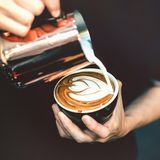 Krebsrisiko Kaffee? Ein Barista schüttet Milch in eine Tasse mit Kaffee