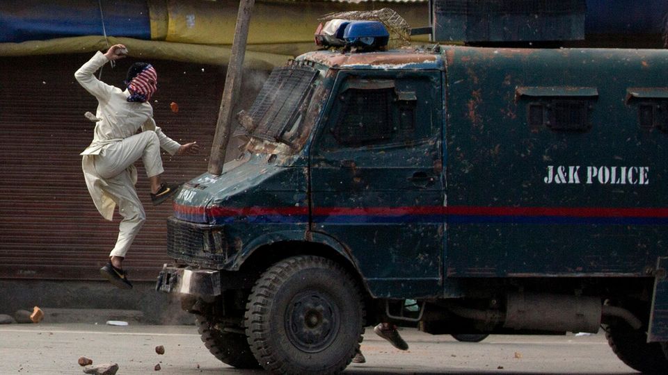 Ein maskierter Demonstrant springt auf ein gepanzertes Polizeifahrzeug, als er bei Protesten in dem von Indien kontrollierten Kaschmir Steine auf das Fahrzeug wirft. 