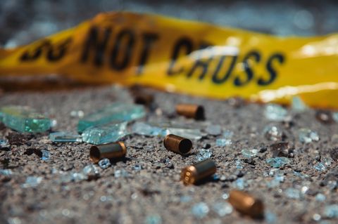 Leere Patronenhülsen und Glassplitter liegen auf dem Asphalt – im Hintergrund: ein Absperrband der Polizei