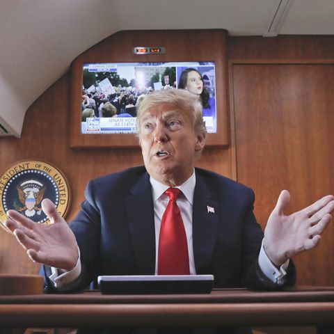 Donald Trump vor laufendem Fernseher in der Präsidentenmaschine Air Force One