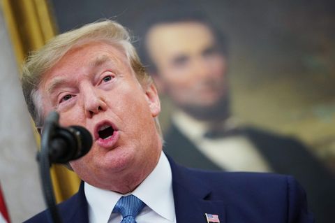 Donald Trump spricht in ein schwarzes Mikrofon. Unscharf im Hintergrund ist ein Ölgemälde von Abraham Lincoln zu sehen