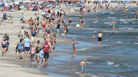 An einem Strand spazieren Badegäste an der Wasserkante entlang. Einige baden in der Ostsee