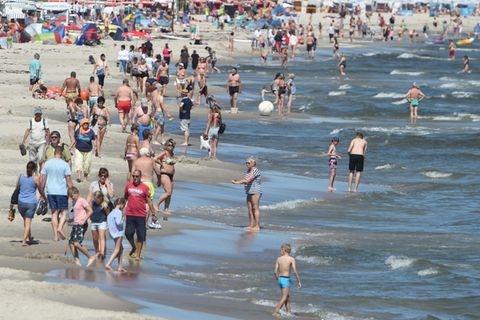 An einem Strand spazieren Badegäste an der Wasserkante entlang. Einige baden in der Ostsee
