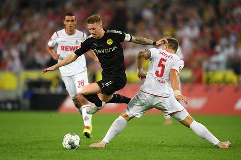Marco Reus stürmt im schwarzen BVB-Dress mit Ball zwischen zwei Kölner Spielern in weiß hindurch