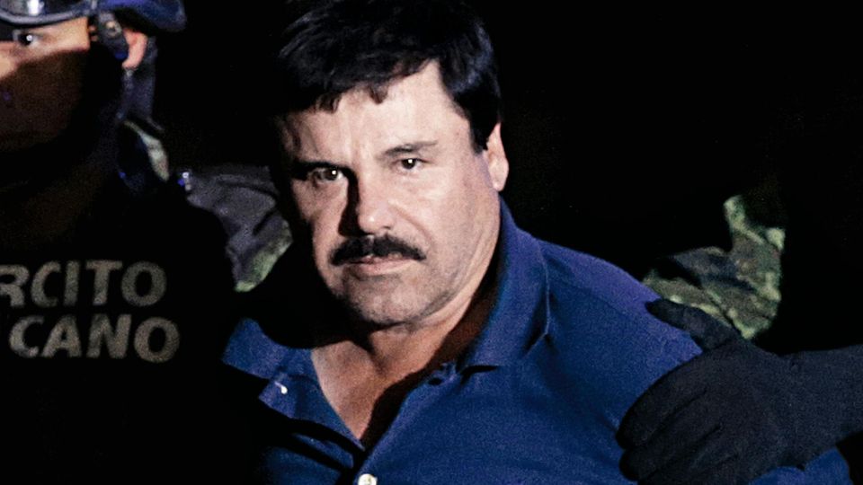 Joaquín Guzmán wird von zwei Mitgliedern der Spezialeinheiten abgeführt. Er blickt mit ernster Miene direkt in die Kamera.