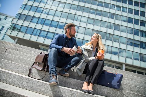 Mann und Frau sitzen vor einem Bürogebäude auf einer Treppe
