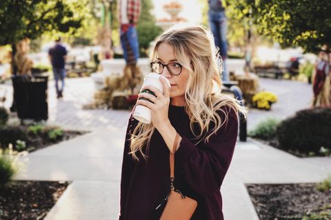 Ein Frau steht allein auf einem Weg und trinkt Kaffee