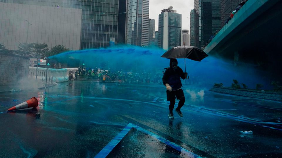 Ein Demonstrant bringt sich vor einem blau gefärbten Wasserstrahl in Sicherheit