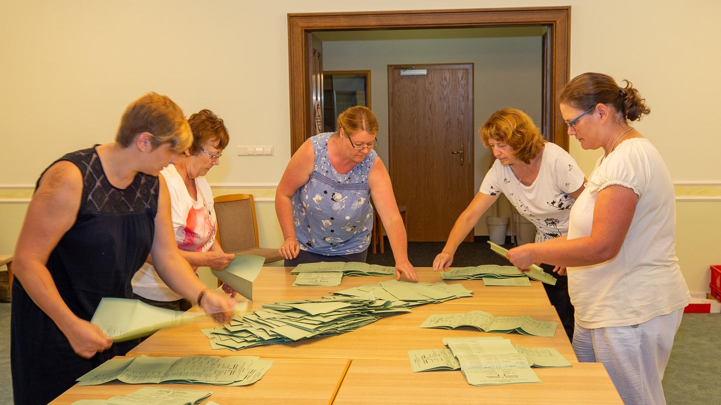 Fünf Frauen beugen sich über zusammengestellte Tische, auf denen hellgrüne Wahlzettel liegen