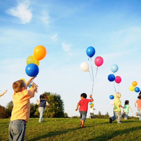 Kinder rennen mit Luftballons über eine Wiese