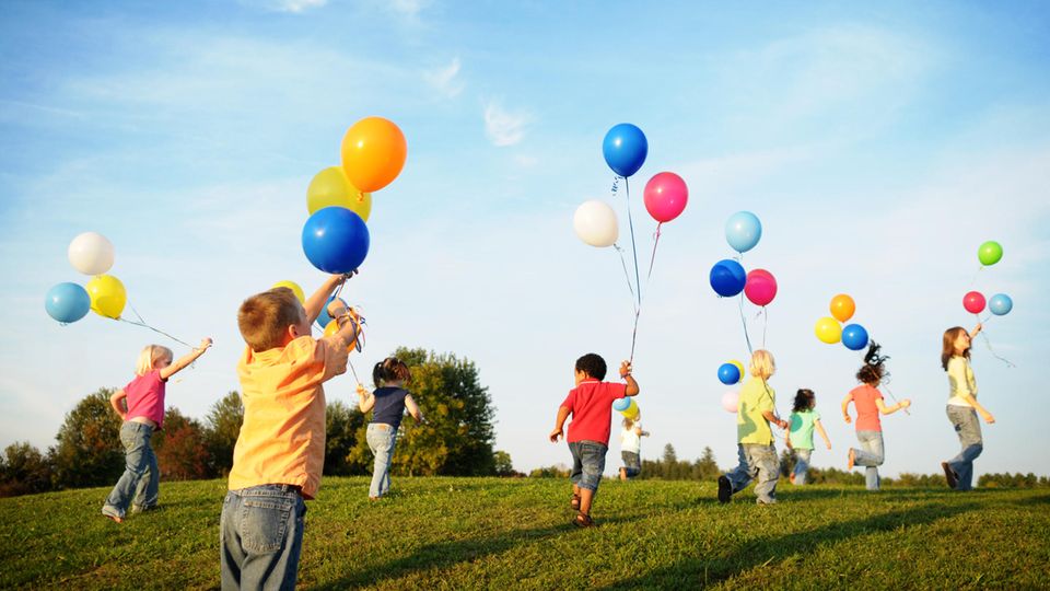 In Gütersloh sind Luftballons bei städtischen Veranstaltungen verboten Kinder rennen mit Luftballons über eine Wiese