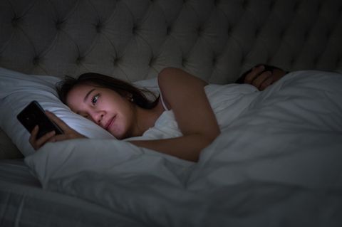 Eine Frau schaut nachts im Bett auf ihr Handy, der Mann schläft