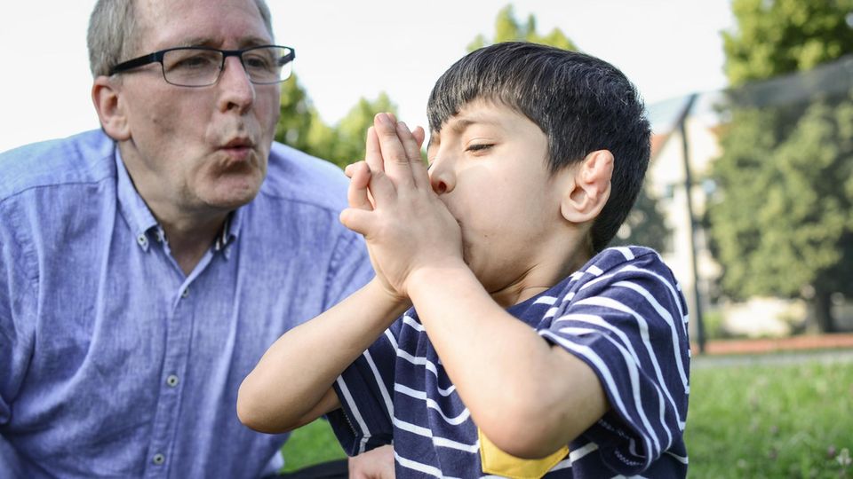 Auf der Wiese neben der neuen Unterkunft zeigt Gammel Khairi, wie man auf einem Grashalm pfeifen kann