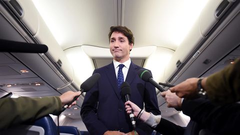 Ein Mann im Anzug steht im Mittelgang eine Flugzeuges und spricht in vier Mikrofone, die ihm Reporter hinhalten