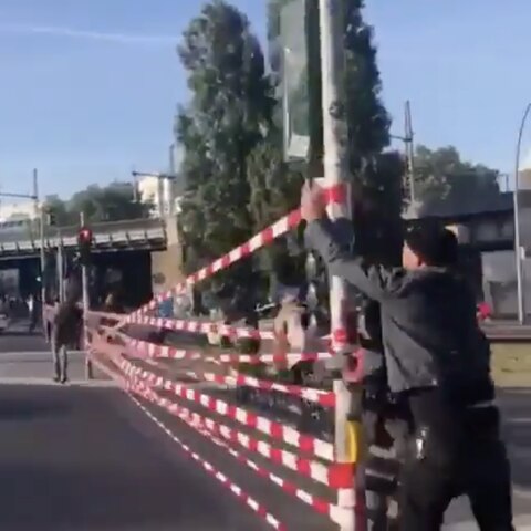 Aktivisten von "Extinction Rebellion" spannen Flatterband zwischen Ampeln in Berlin und sperren so eine Straße am Alexanderplatz