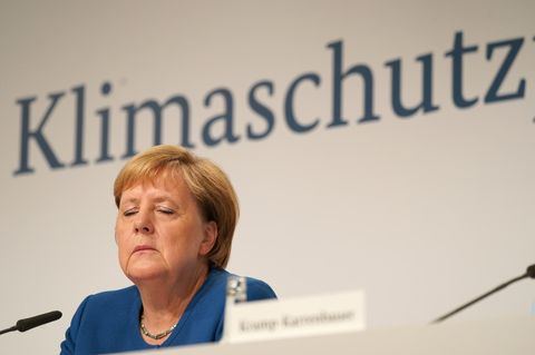 Bundeskanzlerin Angela Merkel sitzt im blauen Blazer und mit geschlossenen Augen auf einem Podium unter dem Wort "Klimaschutz"