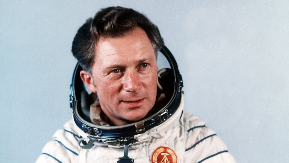 Sigmund Jähn Ein Mann mit Seitenscheitel posiert in einem Weltraumanzug mit DDR-Wappen für ein Foto