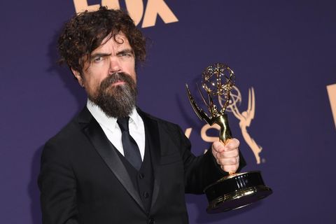 Ein kleinwüchsiger Mann mit dunklen Locken und Vollbart hält einen goldenen US-Fernsehpreis in der linken Hand