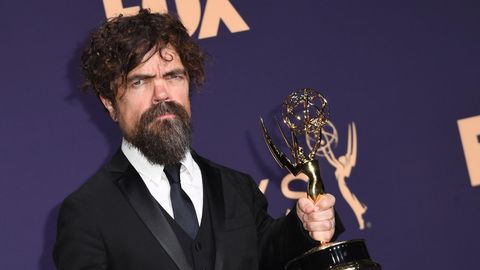 Ein kleinwüchsiger Mann mit dunklen Locken und Vollbart hält einen goldenen US-Fernsehpreis in der linken Hand
