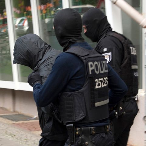 Zwie vermummte Polizisten in dunkelblauer Kampfmontur führen einen Mann ab, der sich seine Kapuze übergezogen hat