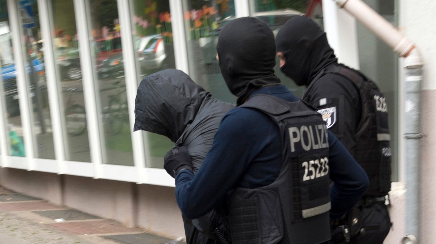 Zwie vermummte Polizisten in dunkelblauer Kampfmontur führen einen Mann ab, der sich seine Kapuze übergezogen hat