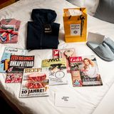 Rundumversorgung: Die Buddies finden auf ihren Zimmern alles, was sie für ein aufregendes, sportliches und entspanntes Wochenende brauchen: Ein kariertes Hemd von Ernsting's Family, eine recycelbare Outdoorjacke der Linie "Pack and Go" von Jack Wolfskin, ein Reiseset von Acqua di Parma und flauschige Hausschuhe von GANT, nebst erstklassiger Lektüre.