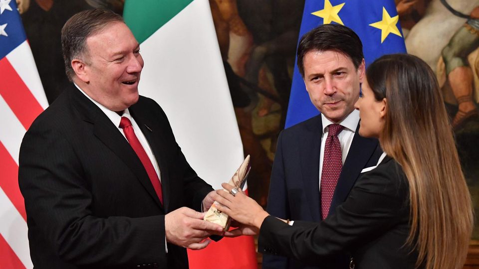 Eine italienische Fernsehreporterin überreicht US-Außenminister Mike Pompeo ein Stück Käse. Eine italienische Fernsehreporterin überreicht US-Außenminister Mike Pompeo ein Stück Käse.