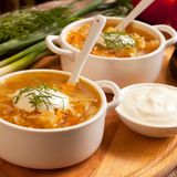 Sauerkrautsuppe mit Rotbarsch im Bierteig  Zutaten:  Suppe: 100 g Zwiebeln, in Streifen geschnitten, insgesamt 80 g kalte Butter, gewürfelt, 200 g Sauerkraut, 50 ml Honig, 200 ml helles Bier, z.B. "Kölsch", 800 ml Geflügelfond, 1 Lorbeerblatt, 200 g mehlig kochende Kartoffeln, geschält und zentimetergroß gewürfelt, 1 kleine frische Knoblauchzehe, abgezogen, 100 g säuerliche Äpfel, geschält, entkernt und klein geschnitten, Meersalz  Teig: 150 ml Bier, z.B. "Rauchbier", 150 g Mehl, Typ 405, 2 Eigelbe (L), 2 Eiklar (L), 1 Messerspitzen Salz, 1 TL Zucker  Fisch: 500 g Rotbarschfilet, 3 cm groß gewürfelt, 10 ml Zitronensaft, Piment D'Espelette, ersatzweise scharfes Paprikapulver, feines Meersalz, ca. 20 g Mehl zum Wenden, 1,5 l Erdnussöl zum Ausbacken  Zubereitung:   Die Zwiebeln in einem Topf in 40 g Butter anschwitzen. Sauerkraut dazugeben und mit anschwitzen, dann mit Honig glasieren. Anschließend mit Bier ablöschen, mit Fond auffüllen und zusammen mit dem Lorbeerblatt sowie den Kartoffeln 60 Minuten zugedeckt bei kleiner Hitze kochen.  Den Lorbeer entfernen und etwas Sauerkraut als Einlage abnehmen. Die Suppe mit dem Knoblauch sowie dem Apfel pürieren und durch ein feines Sieb passieren. Zum Servieren mit Salz abschmecken und mit den restlichen Butterwürfeln aufmixen.  Für den Teig das Bier mit Mehl und Eigelben glatt rühren. Die Eiklar mit Salz steif schlagen, dann den Zucker einrieseln lassen. Den Eischnee mit einem Löffel unter die Biermischung heben.  Fisch mit Zitronensaft beträufeln, mit Piment D'Espelette bestreuen und salzen, dann zu vier Spieße stecken: diese erst in Mehl wenden, dann durch den Teig ziehen und in 175°C heißem Öl 2-3 Minuten knusprig ausbacken. Anschließend herausnehmen und auf Küchenkrepp abtropfen lassen.  Zusammen mit der Suppe servieren.