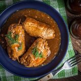 Rinderrouladen für 4 Portionen  Zutaten:  4 große Rinderfleisch-Scheiben aus der Oberschale Salz, Pfeffer, 4 TL Senf, 8 Scheiben Schweinespeck, 4 Gewürzgurken, 100g Schinkenwürfel, etwas Öl, Rotwein, 2 Zwiebeln, 1 Zehe Knoblauch, 1 EL Butter, 1 Lorbeerblatt, 250ml Rinderfond, Etwas Stärke (z.B. Kartoffelmehl), Zubereitungshilfen: Fleischklopfer und Küchengarn  Zubereitung:  Fleischscheiben mit dem Fleischklopfer bearbeiten, salzen und pfeffern und ca. 1 TL Senf auf jeder Scheibe verstreichen. Zwei Scheiben Speck auf jedem Fleischstück auslegen. Gewürzgurke in Scheiben schneiden und mit einigen Schinkenwürfeln auf der Roulade platzieren. Roulade zusammenzurollen und dabei die Füllung umwickeln. Mit etwa einem halben Meter Küchengarn die einzelnen Rouladen befestigen.  Bräter mit Öl erhitzen und die Rouladen 10-20 Minuten darin von allen Seiten scharf anbraten. Rouladen herausnehmen, Bratensatz mit Rotwein ablöschen und umrühren. Rouladen erneut in den Topf geben und weiteren Rotwein dazu schütten, sodass die Rouladen ungefähr zur Hälfte in Schmorflüssigkeit schwimmen (ca. 650ml). Wenn die Flüssigkeit kocht, den Herd auf eine niedrige Temperatur stellen.  1-2 kleingeschnittene Zwiebeln und eine gepresste Knoblauchzehe zusammen mit etwas Butter (1EL) und einem Lorbeerblatt in den Bräter geben. Den Deckel auf den Bräter setzen und die Rouladen bei 130 Grad im Ofen etwa 2 Stunden schmoren lassen. Regelmäßig die Rouladen wenden und mit der Flüssigkeit beschöpfen. Nach der Garzeit die Rouladen aus dem Bräter herausnehmen und das Garn lösen. Für die Soße den Fond durch ein Sieb passieren, Fett abschöpfen und in einen Topf geben. Mit Salz und Pfeffer abschmecken. Kalbs- oder Rinderfond hinzugeben, aufkochen lassen und mit Stärke binden. Nun können die Rouladen angerichtet werden.