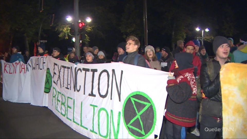 In der Dunkelheit eines Herbstmorgens stehen Demonstranten hinter einem Banner mit dem Schriftzug "Extinction Rebellion"