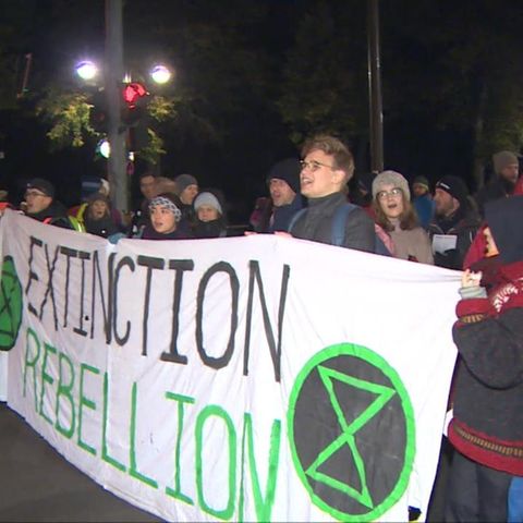 In der Dunkelheit eines Herbstmorgens stehen Demonstranten hinter einem Banner mit dem Schriftzug "Extinction Rebellion"
