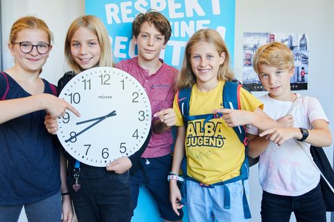 Schüler zeigen auf eine Uhr, die 8.40 Uhr zeigt