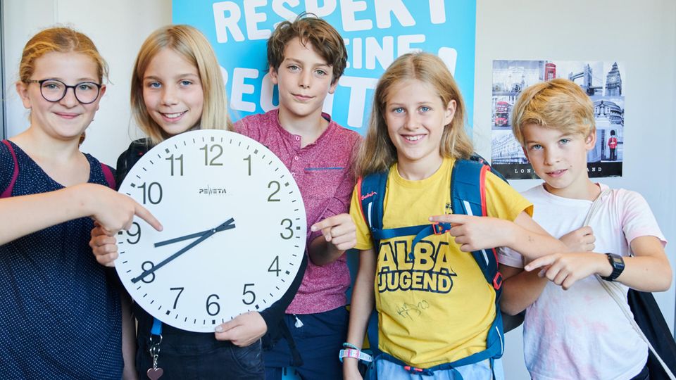 Schüler zeigen auf eine Uhr, die 8.40 Uhr zeigt