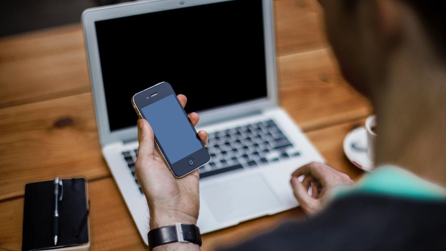 Ein Schüler lernt an seinem Laptop, hat dabei ein Smartphone in der Hand