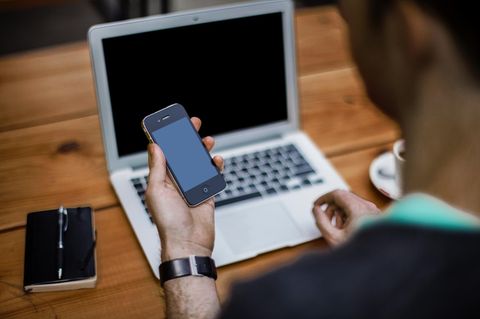 Ein Schüler lernt an seinem Laptop, hat dabei ein Smartphone in der Hand