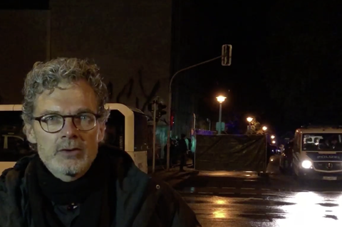 Im Dunkeln steht ein Mann mit Brille und grauen Locken vor einer von der Polizei bewachten Absperrung