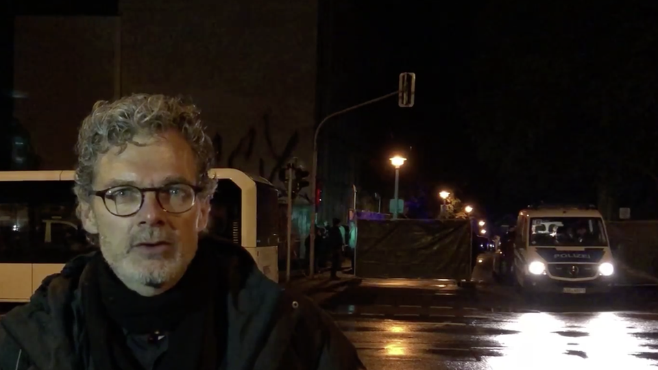 Im Dunkeln steht ein Mann mit Brille und grauen Locken vor einer von der Polizei bewachten Absperrung