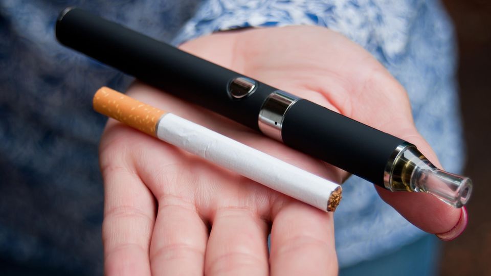 E-Zigarette: Eine Frau hält eine Zigarette und eine E-Zigarette in der Hand