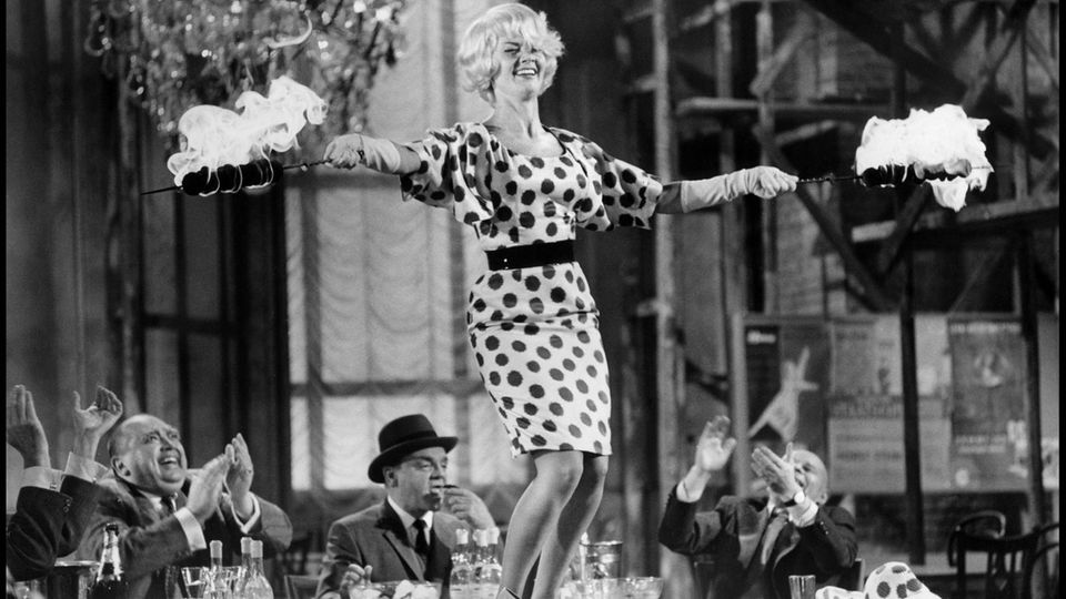 Liselotte Pulver als Sexbombe "Fräulein Ingeborg" in Billy Wilders Ost-West-Satire "Eins, zwei, drei". Die Szene, in der sie die Hüfte schwingend auf dem Tisch tanzte, machte sie zur Schweizer Antwort auf Marilyn Monroe. Der Film brachte der in Bern geborenen Schauspielerin 1961 weltweit Anerkennung ein. Zu dieser Zeit war sie in Deutschland bereits ein Publikumsliebling. Die "Liselotte aus der Schweiz", wie ein Reporter sie nannte, verzückte mit ihrem Charme das Publikum. Ihr ansteckendes Lachen wurde dabei zu Pulvers Markenzeichen.