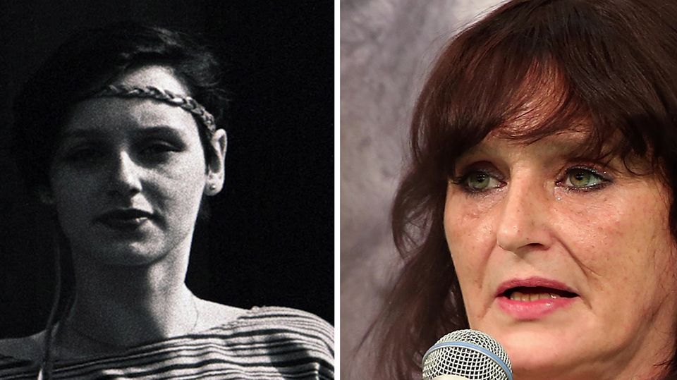 Eine Frau mit rotbraunenlangen Haaren stützt ihren Kopf auf ihre linke Hand. Hinter ihr hängt ein groSchwarz-weiß-Portät von ihr