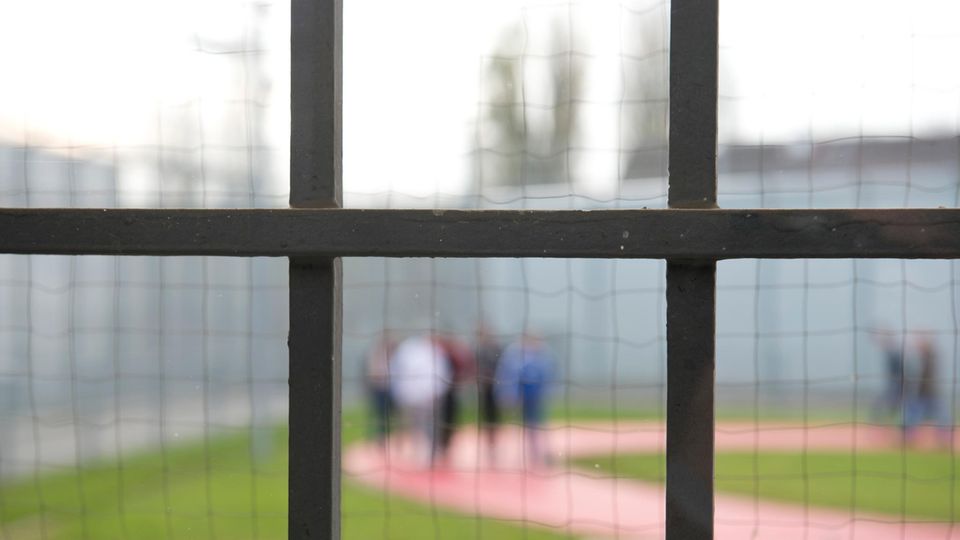 Hinter einem Gitter laufen am Gefängnisinsassen einer Justizvollzugsanstalt
