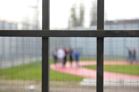 Hinter einem Gitter laufen am Gefängnisinsassen einer Justizvollzugsanstalt