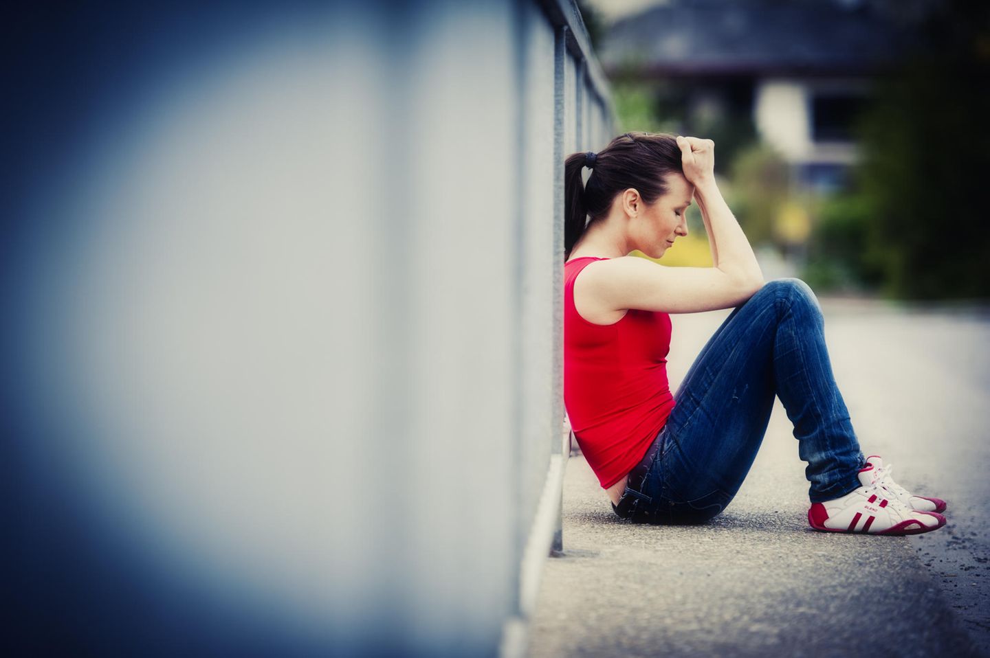 Hochstapler-Syndrom – unglückliche junge Frau sitzt an Brückengeländer