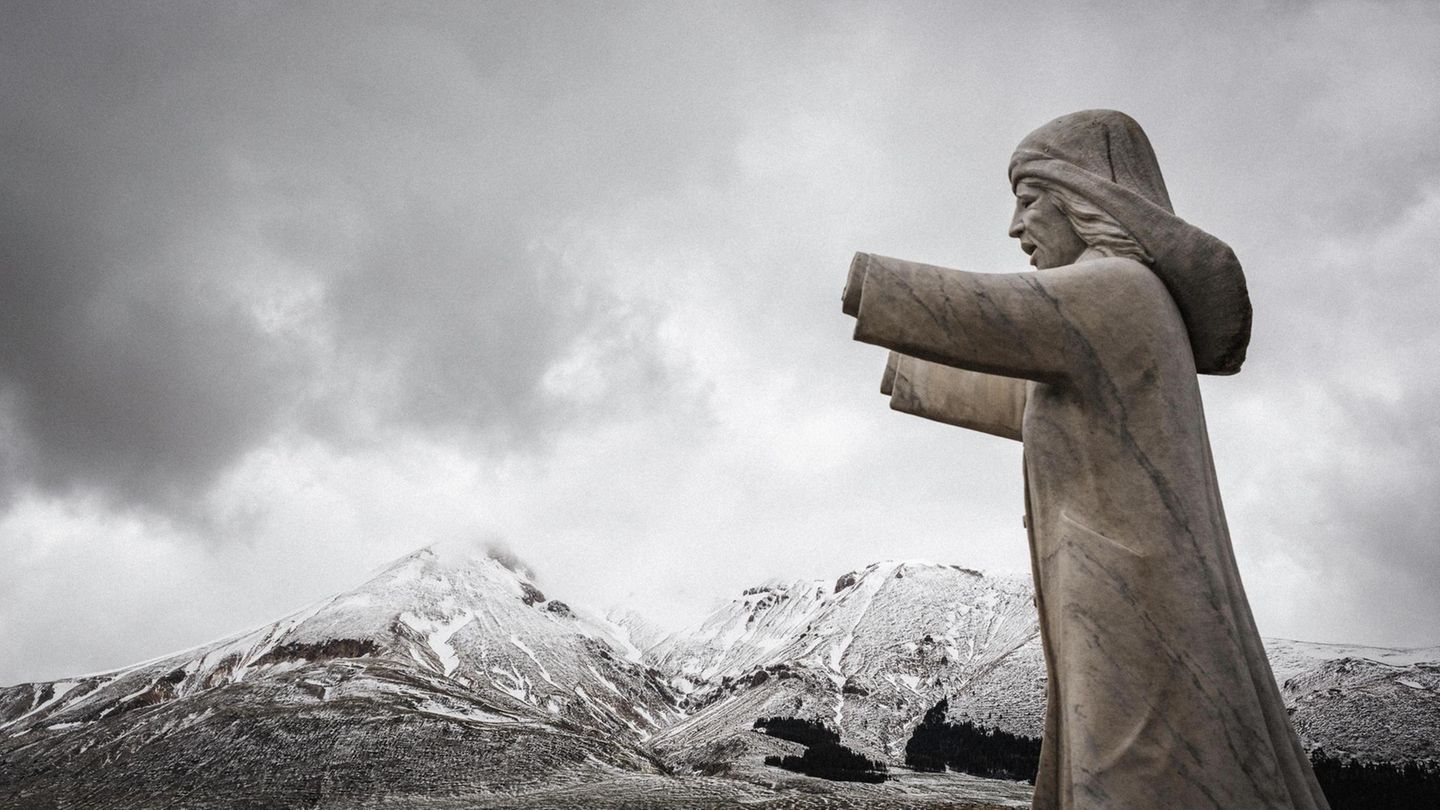 Im Vordergrund: Die Statue einer Frau. Im Hintergrund: Schneebedecktes Gebirge