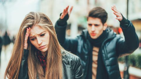 Frau schaut traurig und genervt, während ihr Partner im Hintergrund wütend zu sein scheint